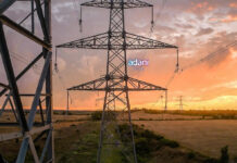 Adani Energy Solutions Q3 FY26 Results: Profit Drops Over 8% to ₹574 Crore on Higher Tax Expenses, Revenue Up 15% High-voltage electricity transmission tower in Indian countryside at sunset, illustrating power infrastructure growth for Adani Energy Solutions